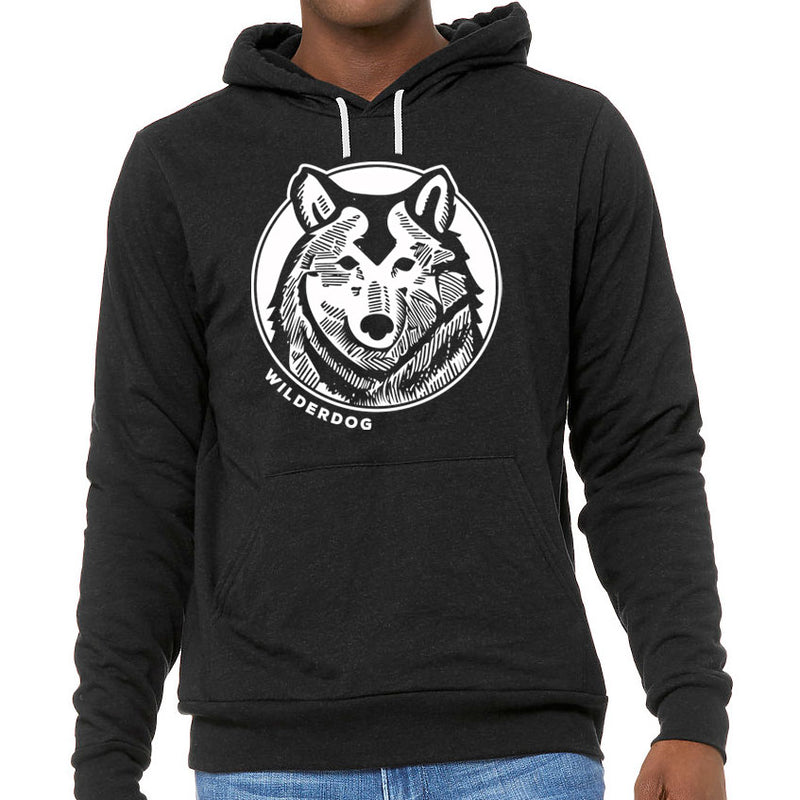 A person wearing the Wilderdog Hoodie, a black unisex sweatshirt featuring a white graphic of a husky dog face inside a circle on the chest, with the word "WILDERDOG" written below the graphic. This ultra-soft hoodie includes a kangaroo pocket and pairs perfectly with blue jeans.